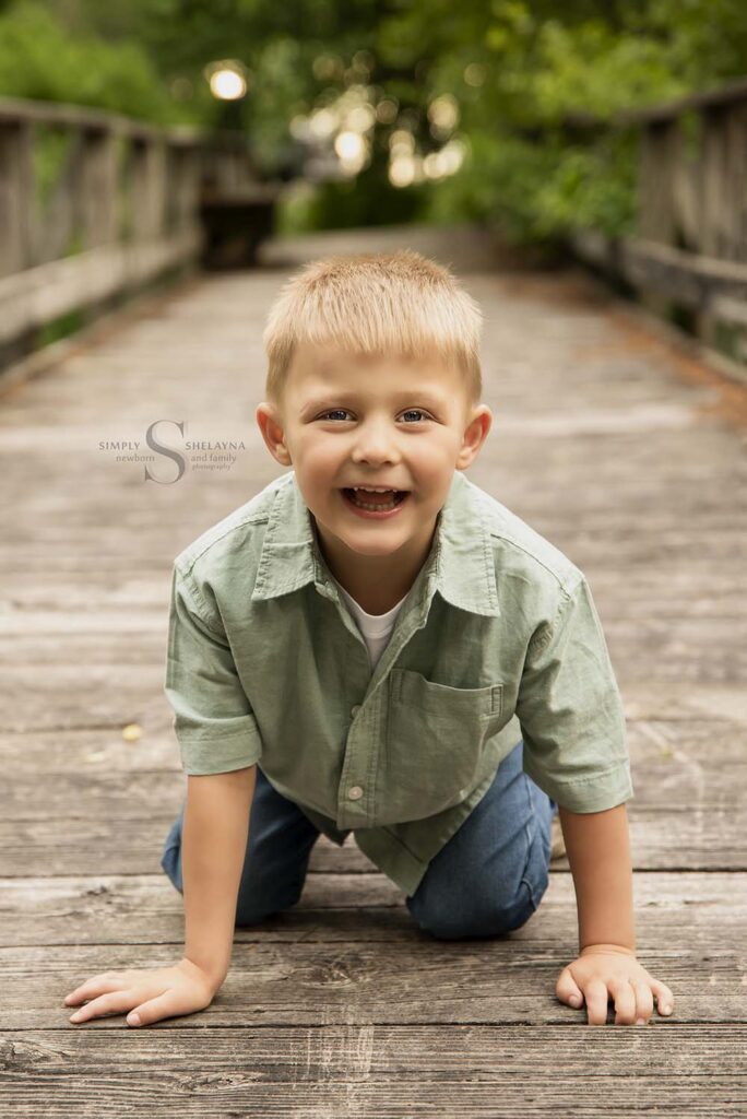 A young boy poses on his hands and knees on a boardwalk in Mexico Point State Park with Simply Shelayna Family Photography in Oswego NY.