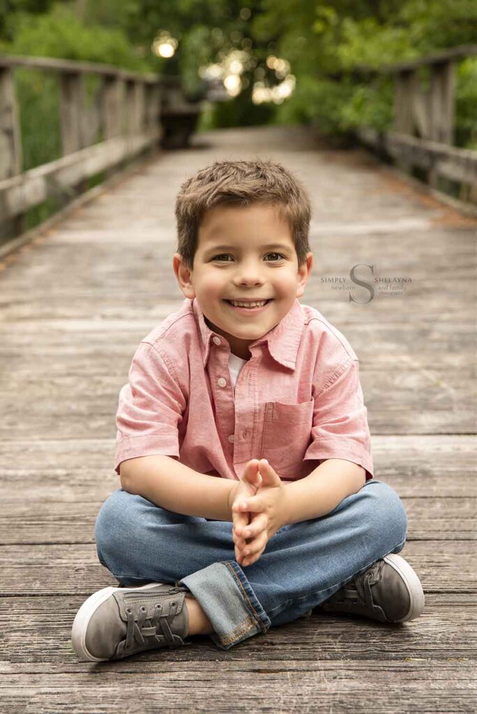 A young boy sits criss cross apple sauce on a board walk bridge with Simply Shelayna Family Photography in Syracuse NY.