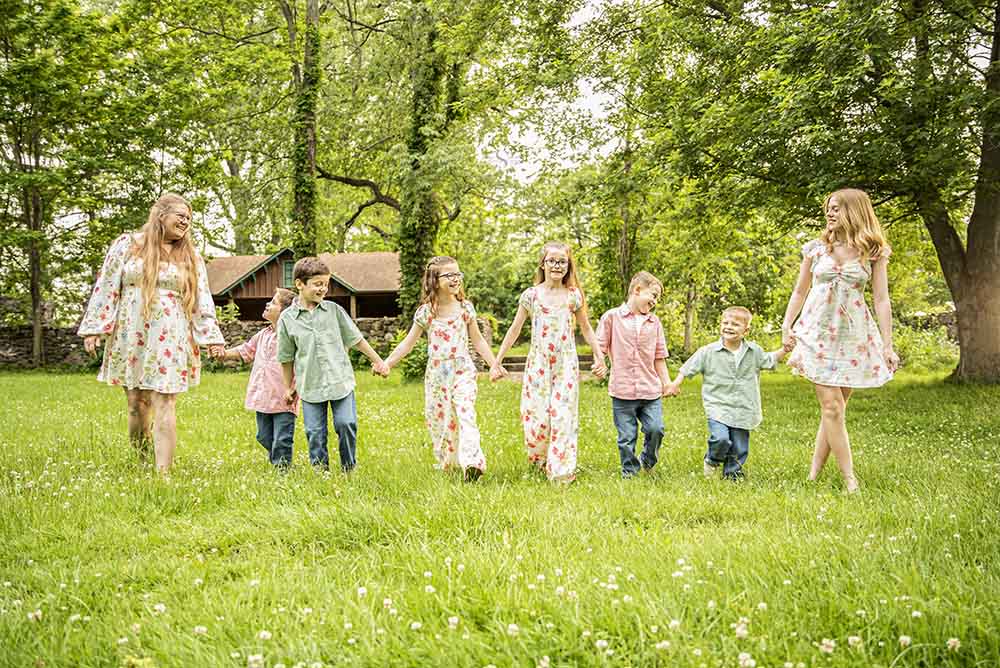 A mother and her 7 children walk in a horizontal line holding hands for a portrait with Simply Shelayna Family Photographer in Oswego NY.
