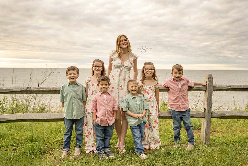 Seven siblings pose for a portrait in front of Lake Ontario at Mexico Point State Park with Simply Shelayna Family Photography in Oswego NY.