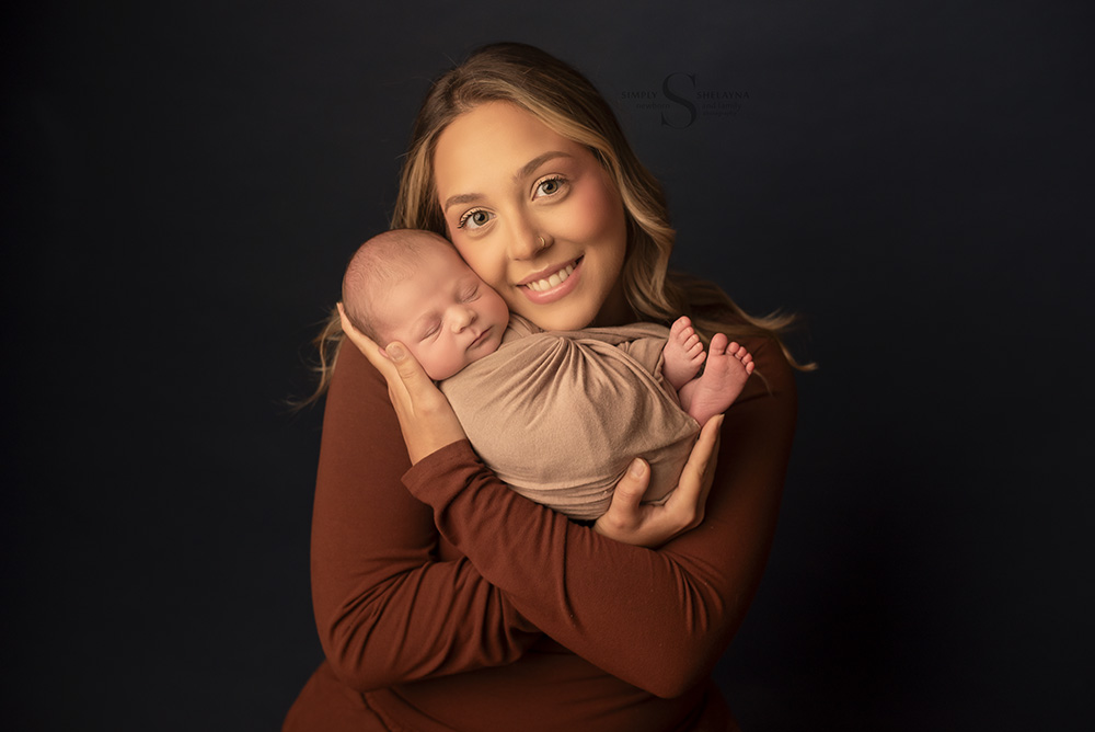 A mother smiles as she embraces her newborn son for a portrait with Simply Shelayna Newborn Photography in Syracuse NY.