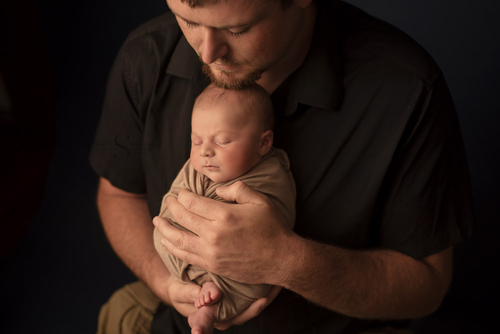 A father holds his son close to his chest for a portrait with Simply Shelayna Newborn Photography in Oswego NY.