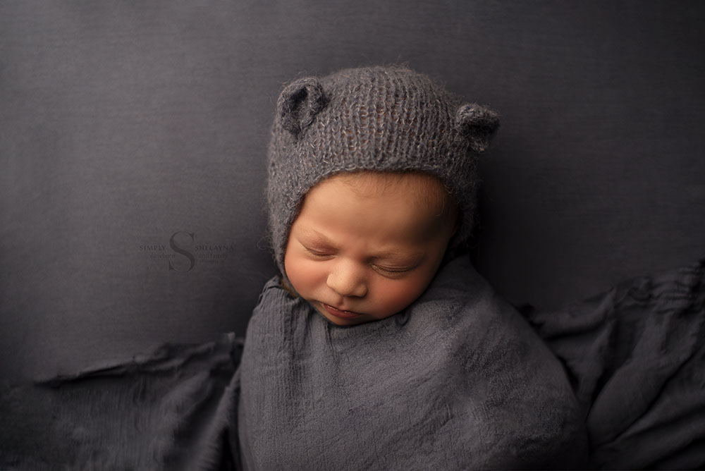 As a blue teddy bear, a baby boy is tucked in for a sleepy portrait with Simply Shelayna Newborn Photography in CNY.
