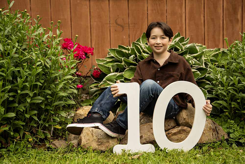 A boy displays his age while sitting by a garden bed with Simply Shelayna Child Photography in Oswego NY.