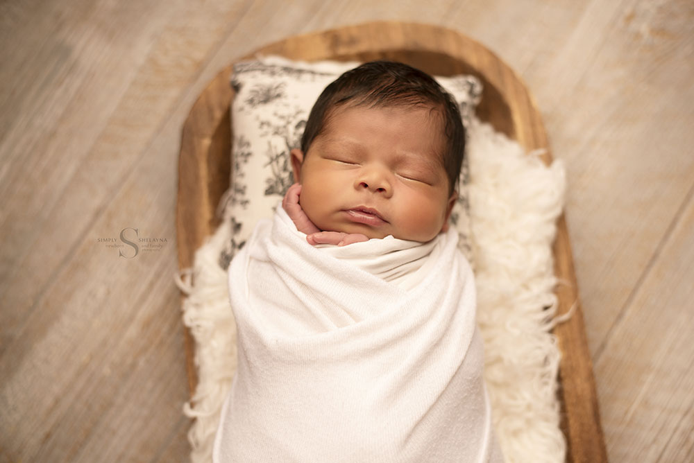 A newborn baby girl sleeps swaddled on a wooden tray with Simply Shelayna Newborn Photography in Oswego NY.