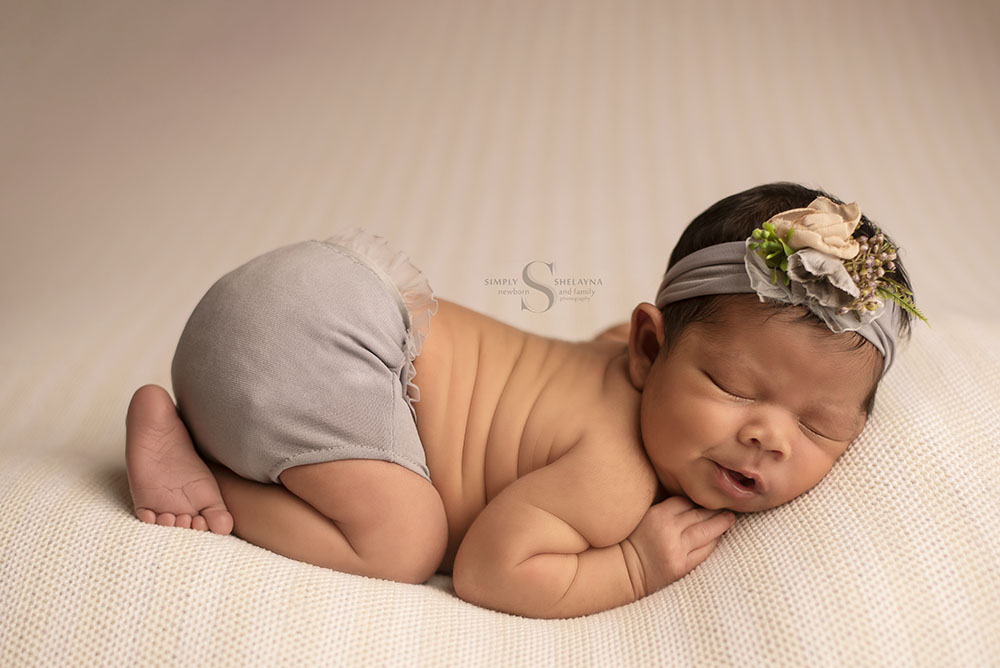 A newborn girl sleeps peacefully in a bum up position for a portrait with Simply Shelayna Newborn Photography in CNY.