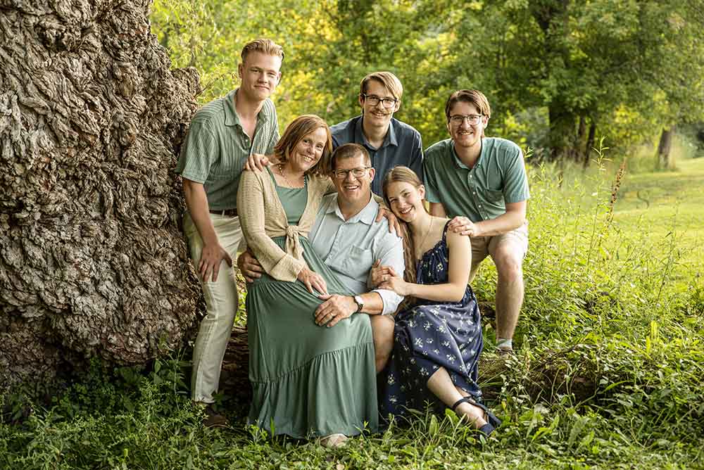 A family of grown up children pose in at an enormous weeping willow at Fall Brook in Oswego NY for family portraits with Simply Shelayna Family Photography.