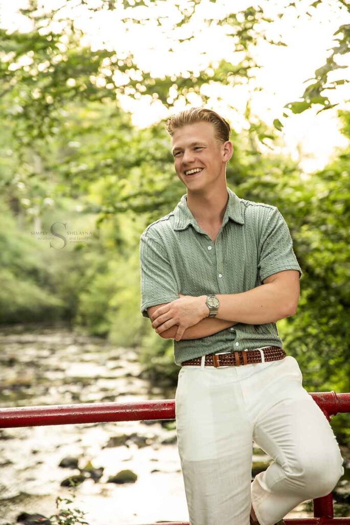 A young man leans up a against a red railing over Fall Brook at Suny Oswego with Simply Shelayna Family Photography in CNY.