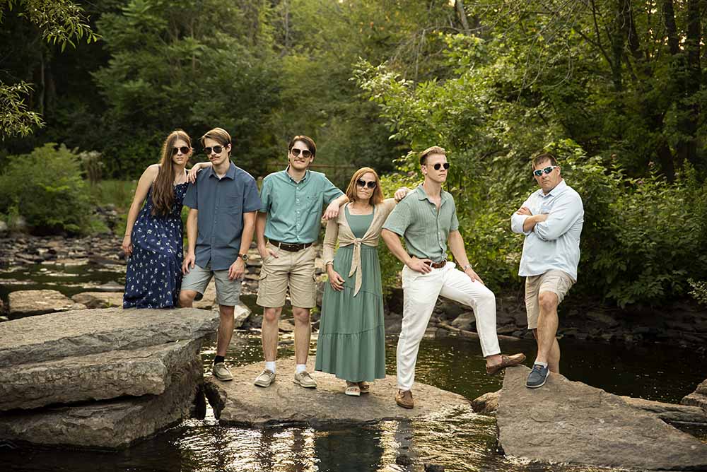 A family of grown up children pose in on large rocks crossing a brook at Fall Brook in Oswego NY for family portraits with Simply Shelayna Family Photography.