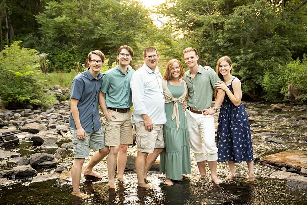 A family of grown up children pose in a shallow brook at Fall Brook in Oswego NY for family portraits with Simply Shelayna Family Photography.