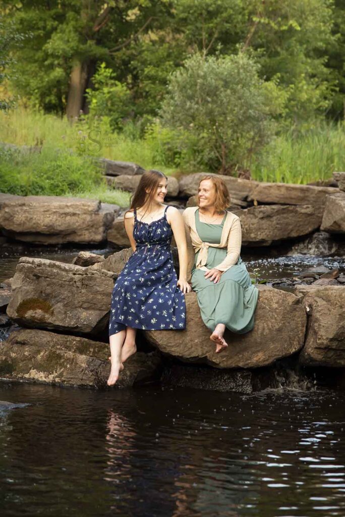 A mother and daughter sit on large rocks by a waterfall at Fall Brook in Oswego NY with Simply Shelayna Family Photography.