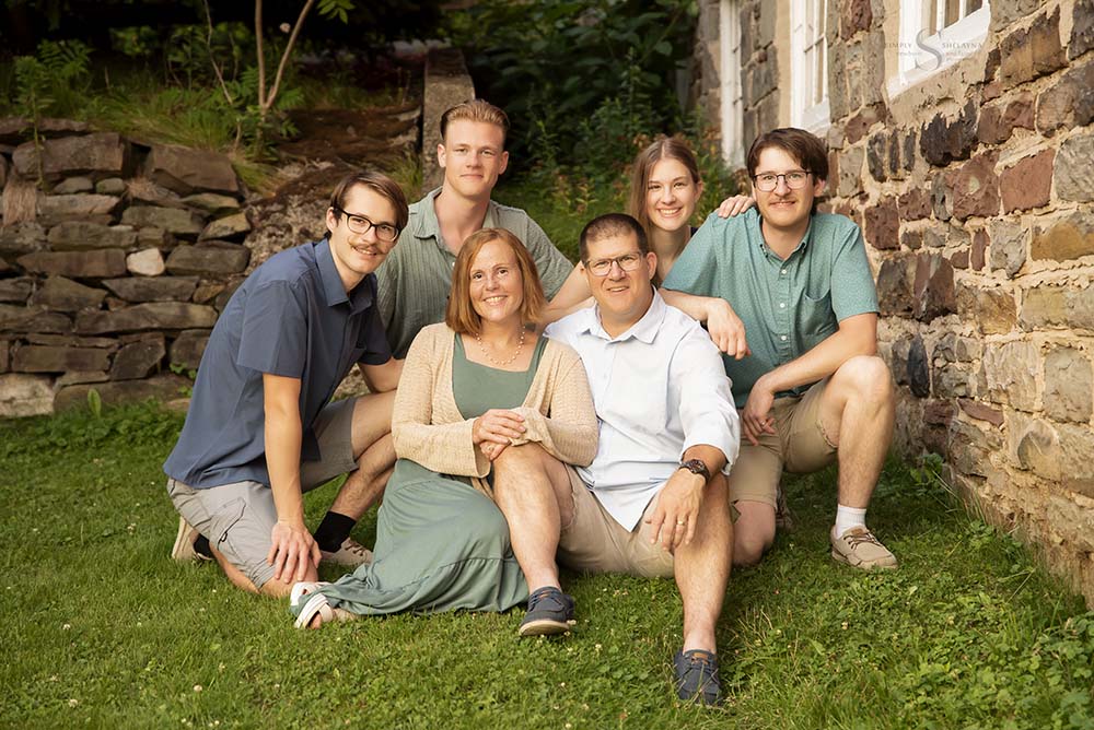 A family of grown up children pose at a stone wall at Fall Brook in Oswego NY for family portraits with Simply Shelayna Family Photography.