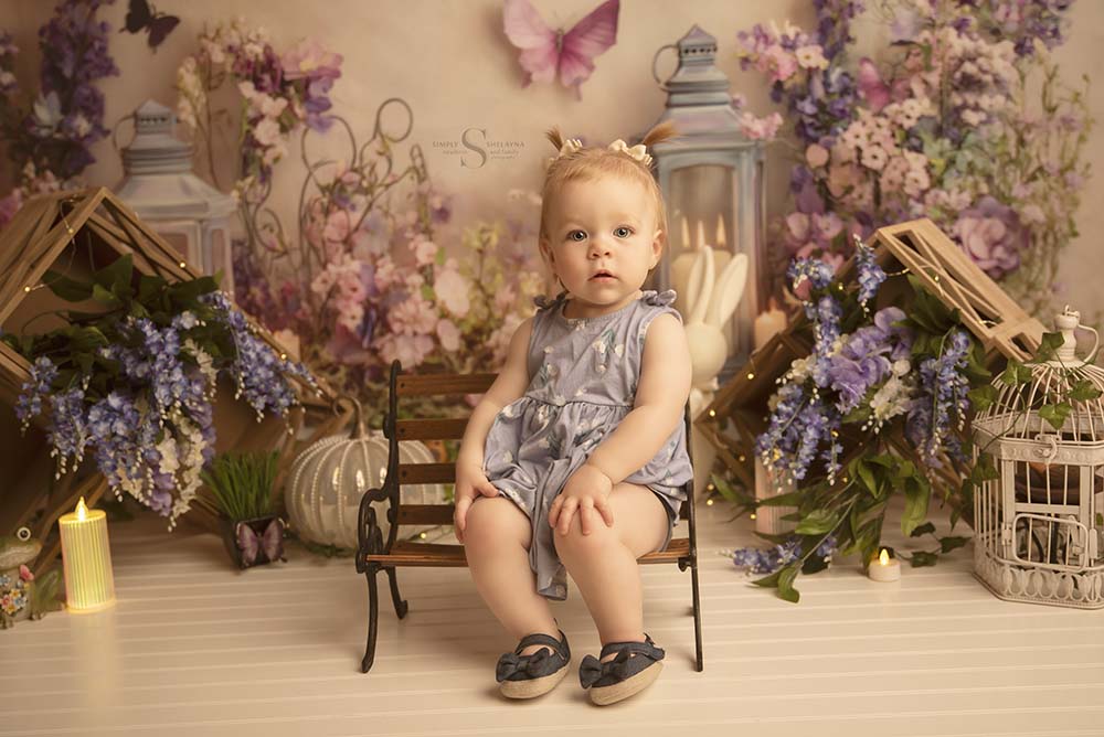 A 1 year old girl sits on a prop bench for a portrait with Milestone Photographer Simply Shelayna in Syracuse NY.