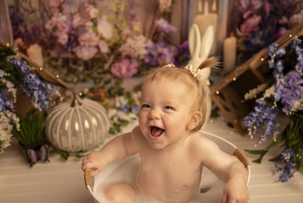 A baby girl gives a big smile in a bubble bath splash with Simply Shelayna Photography's milestone portrait session.