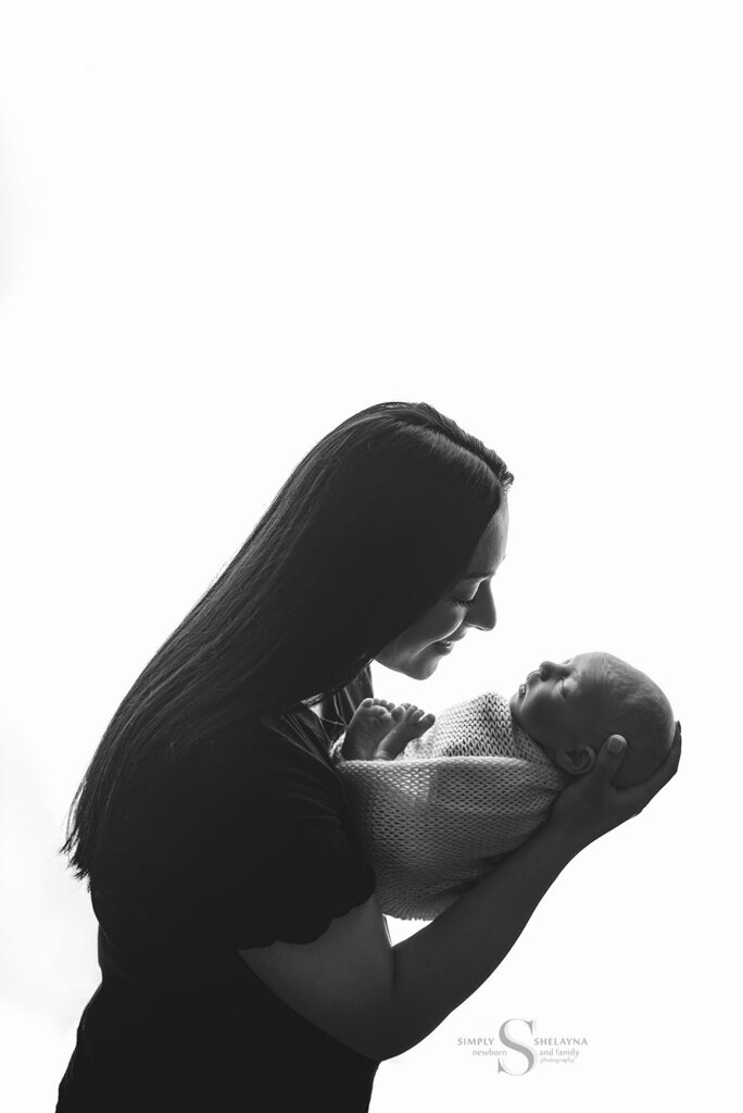 A black and white back lit image of a mother holding her newborn son with Simply Shelayna Newborn Photography in Cicero NY.