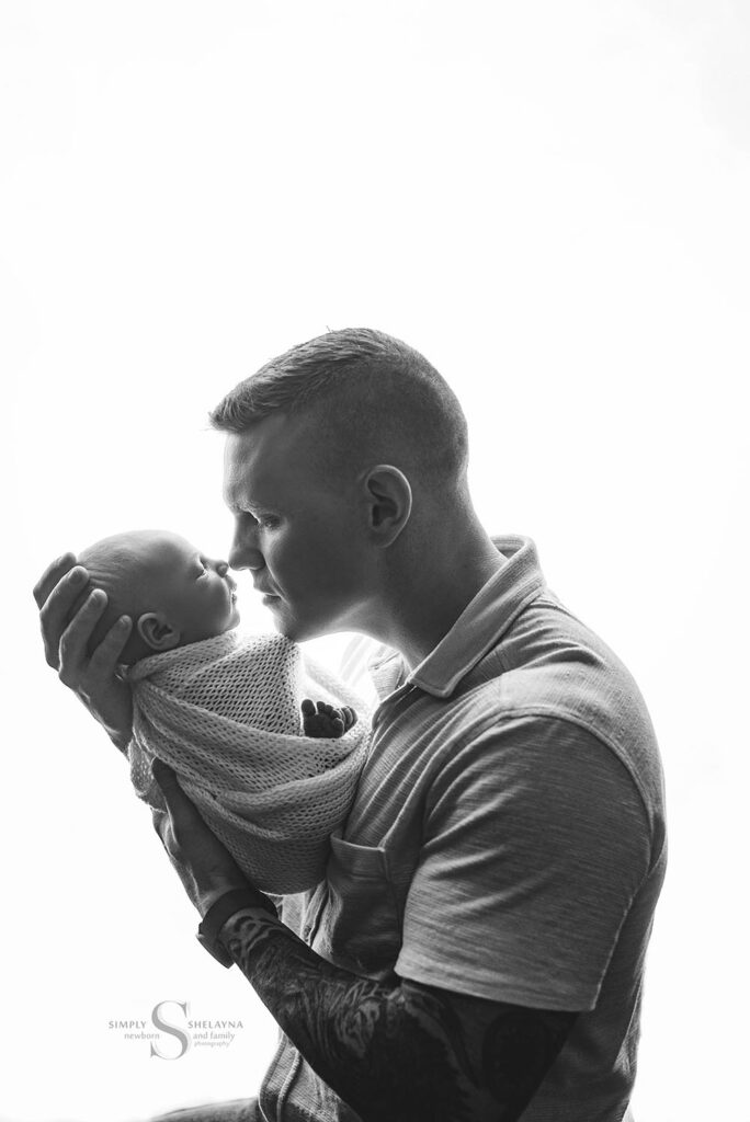A black and white back lit image of a father nuzzling nose to nose with his newborn son with Simply Shelayna Newborn Photography in Cicero NY.