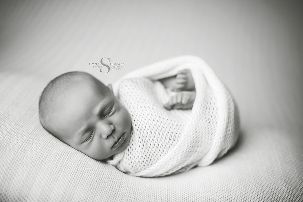 A black and white portrait of a newborn boy swaddled in a hand knitted wrap and bear bonnet with Simply Shelayna Newborn photography in CNY.