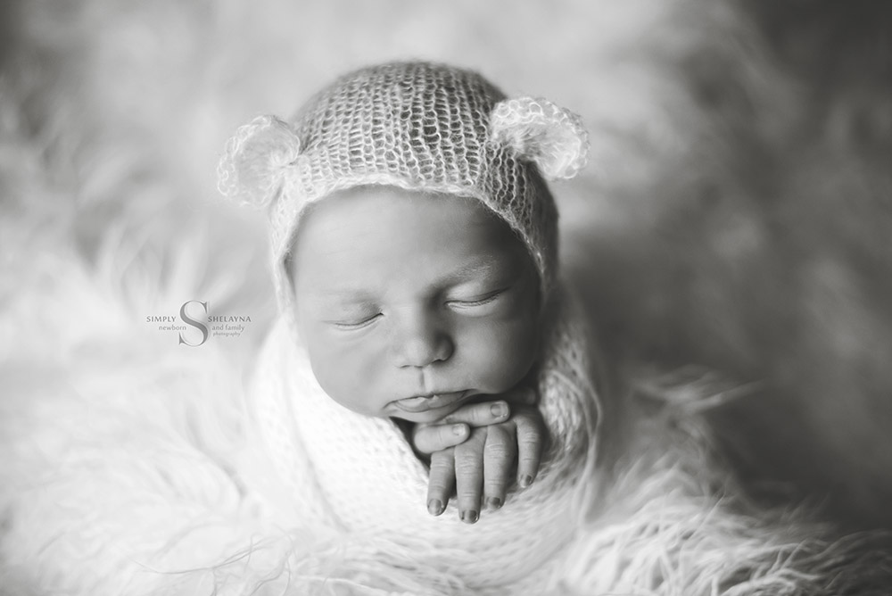 A black and white portrait of a newborn posed in a hand knitted wrap and bear bonnet with Simply Shelayna Newborn photography in CNY.