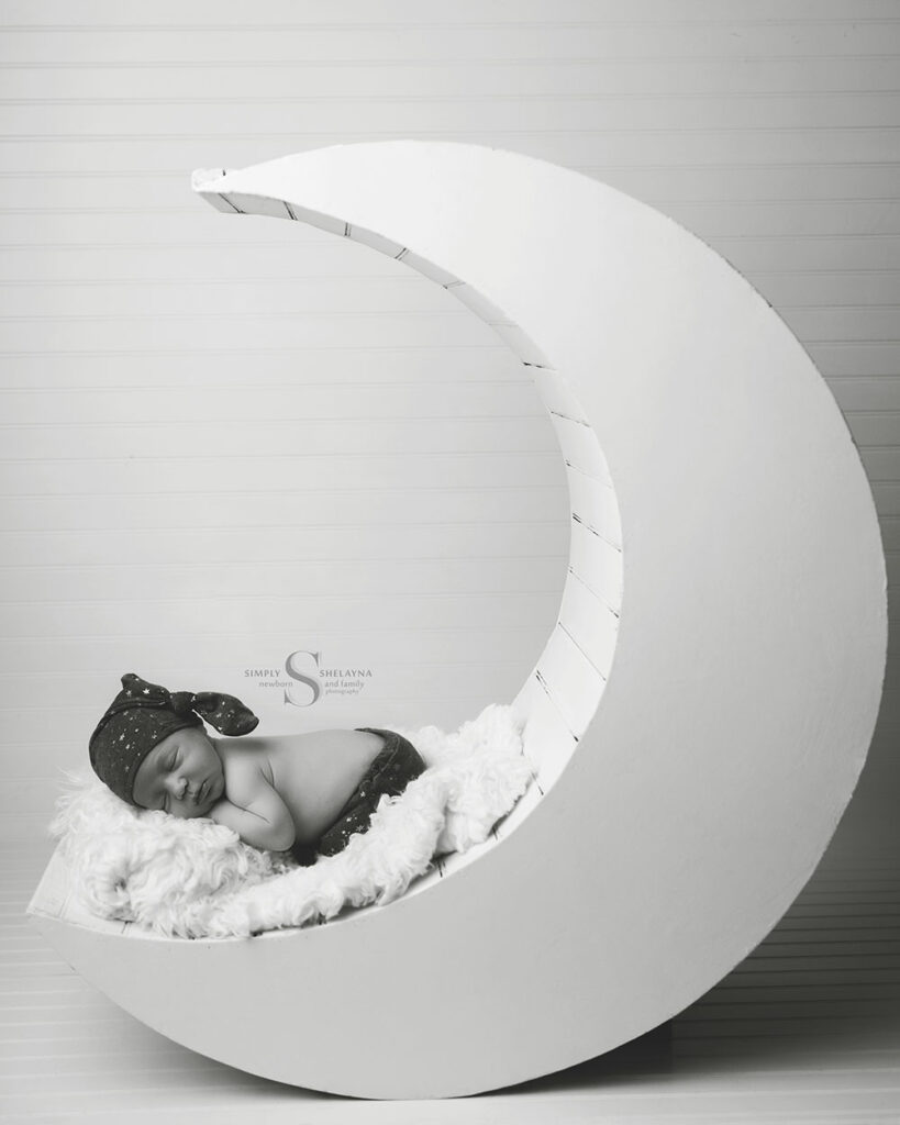 A black and white newborn portrait of a newborn baby sleeping on a large white moon with Simply Shelayna Newborn Photography in Syracuse NY.