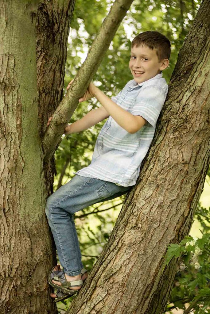 A young boy leans up in a tree for a portrait with Simply Shelayna Photography in CNY.