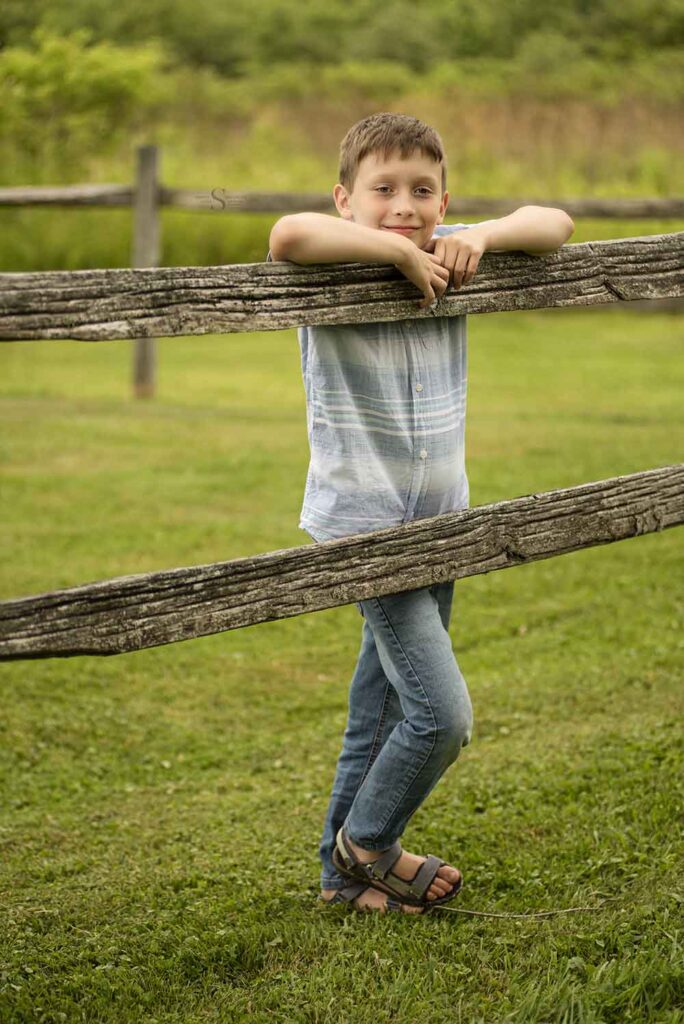 A young boy leans on a wooden fence for a portrait with Simply Shelayna Photography in CNY.