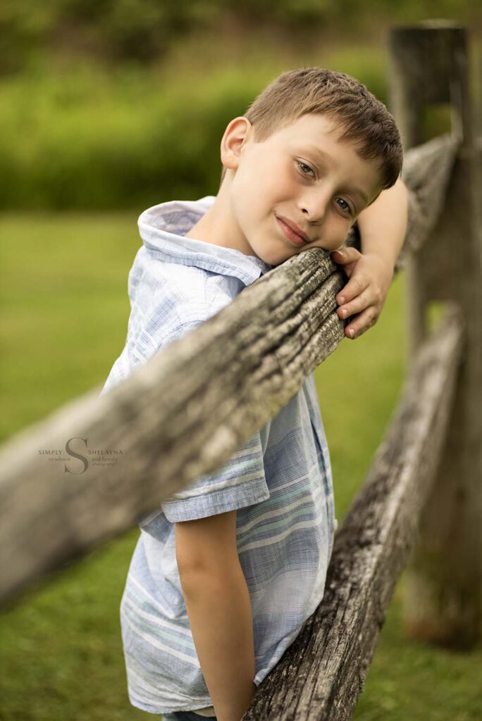 A young boy leans on a wooden fence for a portrait with Simply Shelayna Photography in CNY.