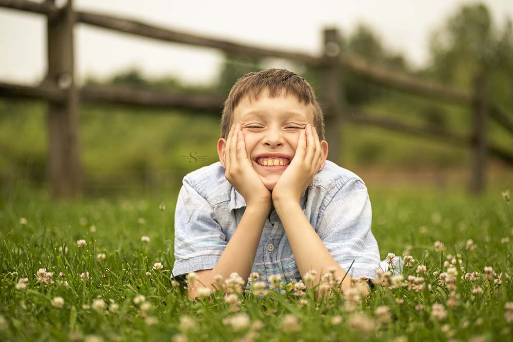 A young boy likes in the grass and flowers for a portrait with Simply Shelayna Family Photography in Syracuse NY.