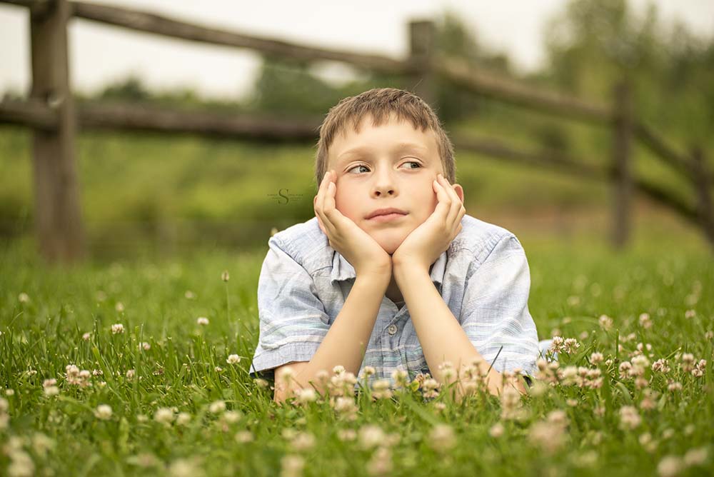 A young boy likes in the grass and flowers for a portrait with Simply Shelayna Family Photography in Syracuse NY.