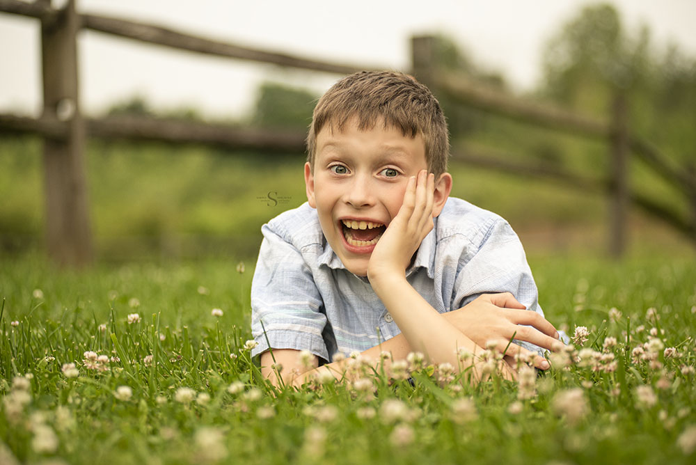 A young boy likes in the grass and flowers for a portrait with Simply Shelayna Family Photography in Syracuse NY.