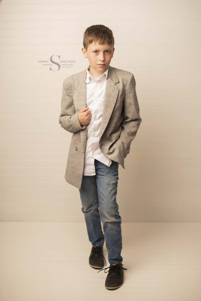 A young boy poses in a suit coat for a portrait with Simply Shelayna Child Photography in Oswego NY.