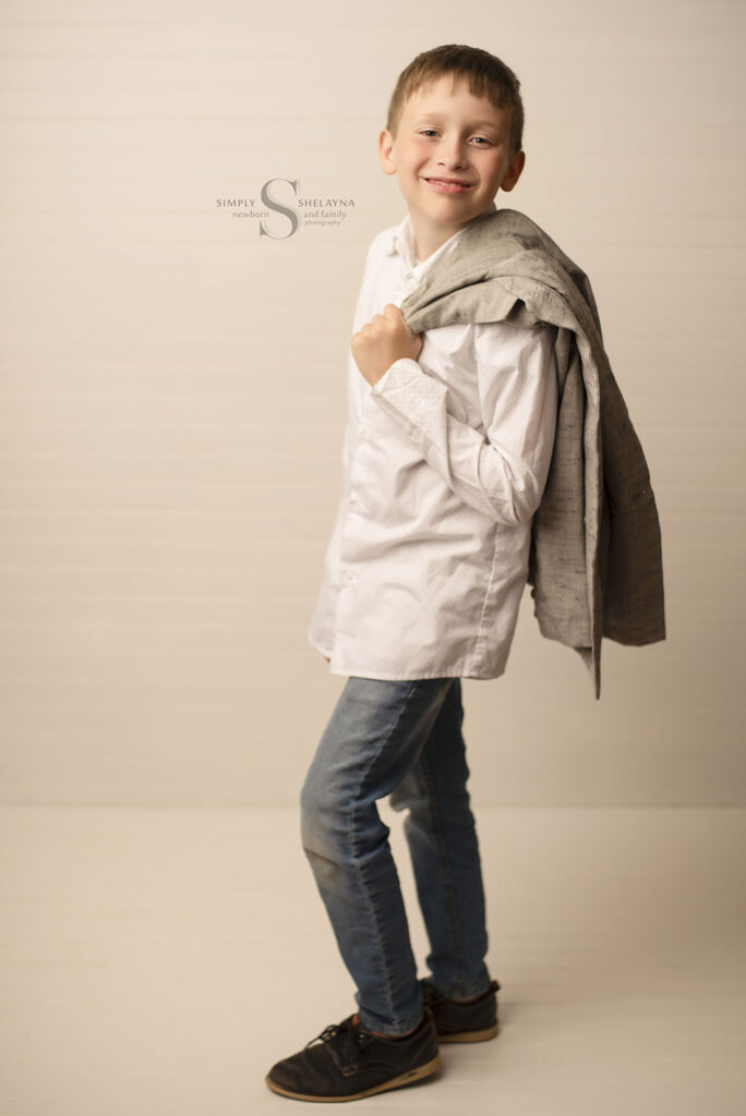 A young man stands with his suit coat draped over his shoulder for a model portrait with Simply Shelayna Child Photography in CNY.