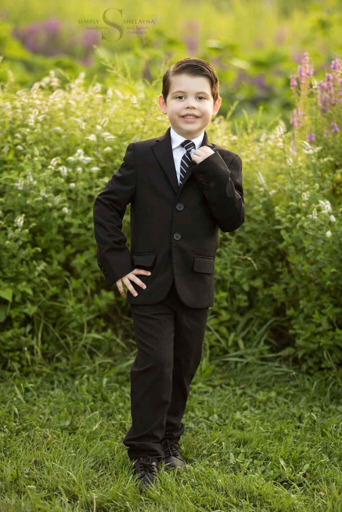 A five year old boy poses in a black suit with Simply Shelayna Child Photography in CNY.