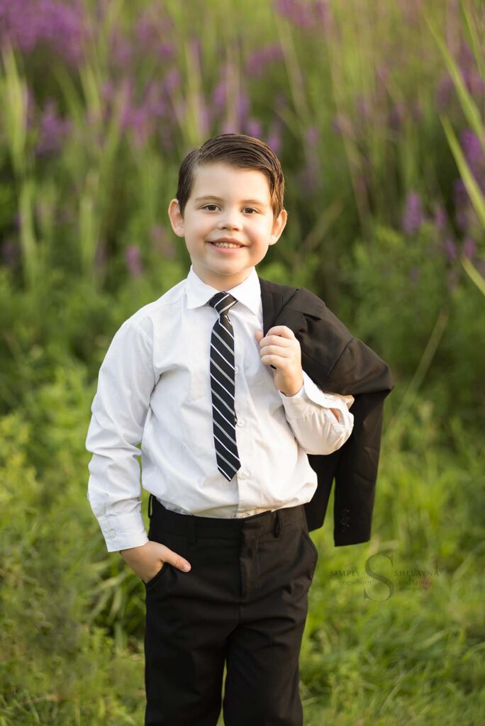 A five year old boy poses in a black suit with Simply Shelayna Child Photography in CNY.