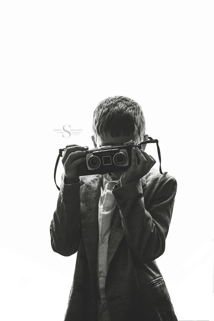 A black and white portrait of a young boy using a vintage 3d camera with Simply Shelayna Photography in Syracuse NY.
